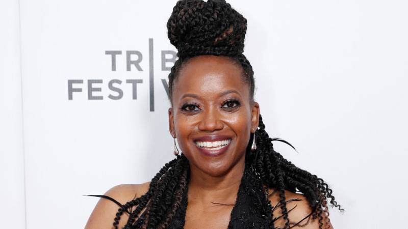 a Black woman smiles at a film festival red carpet against a white backdrop