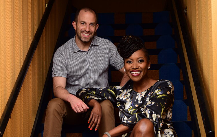 a white man and a Black woman smile in a portrait on a staircase
