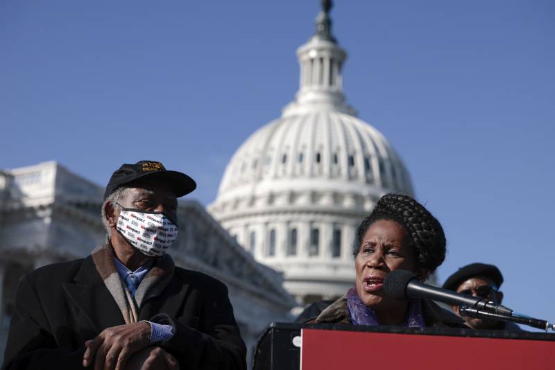 a press conference on Capitol Hill; a Black man stands next to a Black woman speaking at a podium