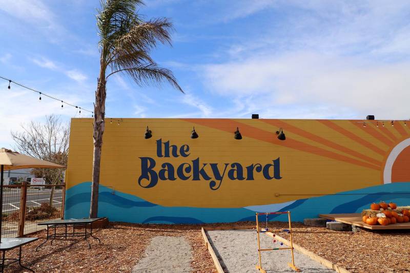 a large mural that reads "the Backyard" is painted on the side of a wall in a large, outdoor space to eat
