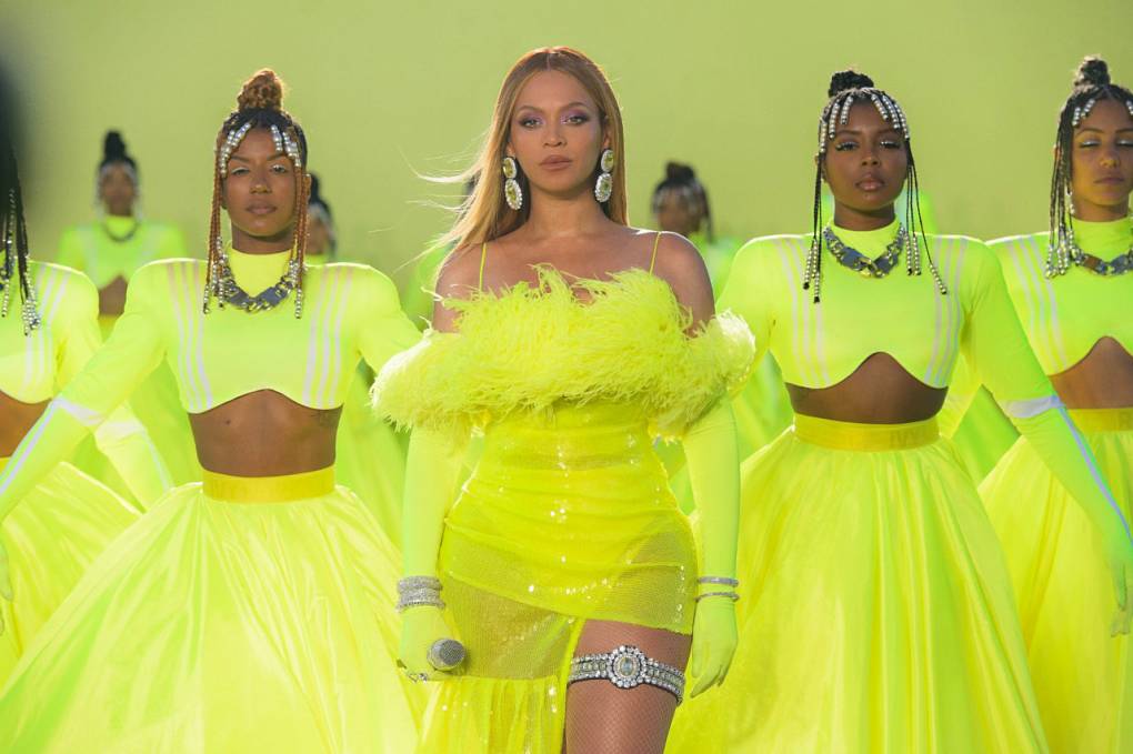 A beautiful Black woman stands in formation with other Black women. They are all wearing flourescent yellow skirts and dresses.
