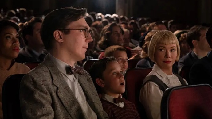 A young boy sits in a packed movie theater between his parents.