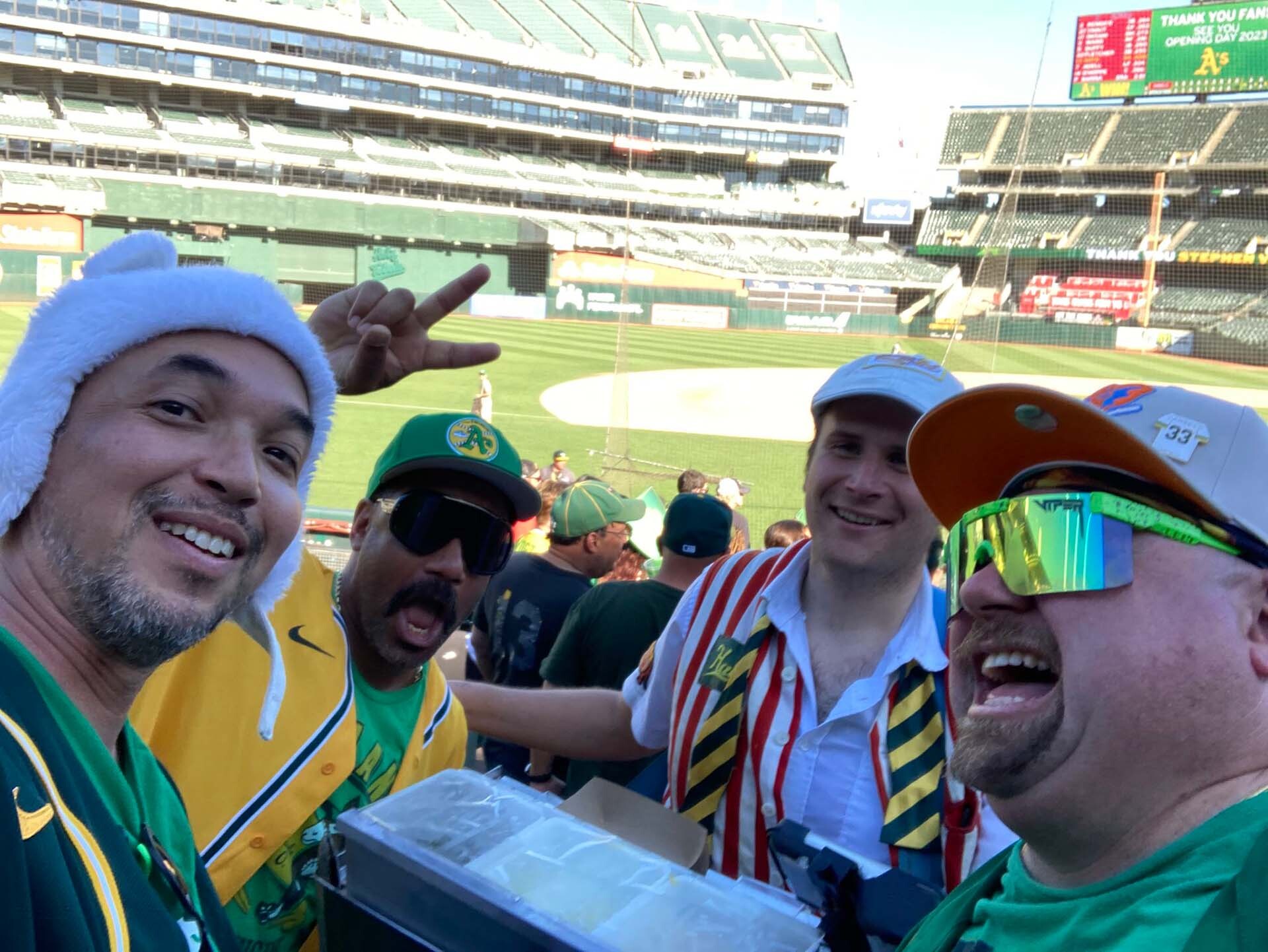 Hot dog vendor holds a tray of condiments surrounded by smiling A's fans.
