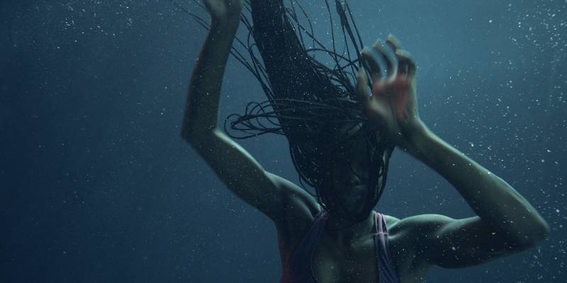 A Black woman floating down under the water, her braids floating up over her head.