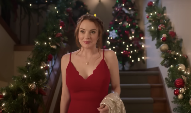 Lindsay Lohan wearing a red dress, walking down some stairs, Christmas decorations all around her.
