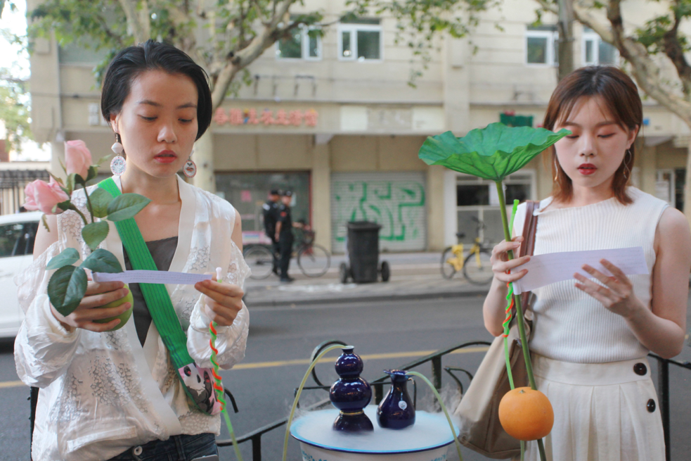Two Asian women in white hold plants and read from strips of paper next to bowl of dry ice