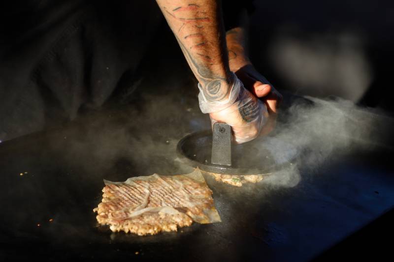 a cook "mashes" a burger patty by flattening it with an iron press on the grill