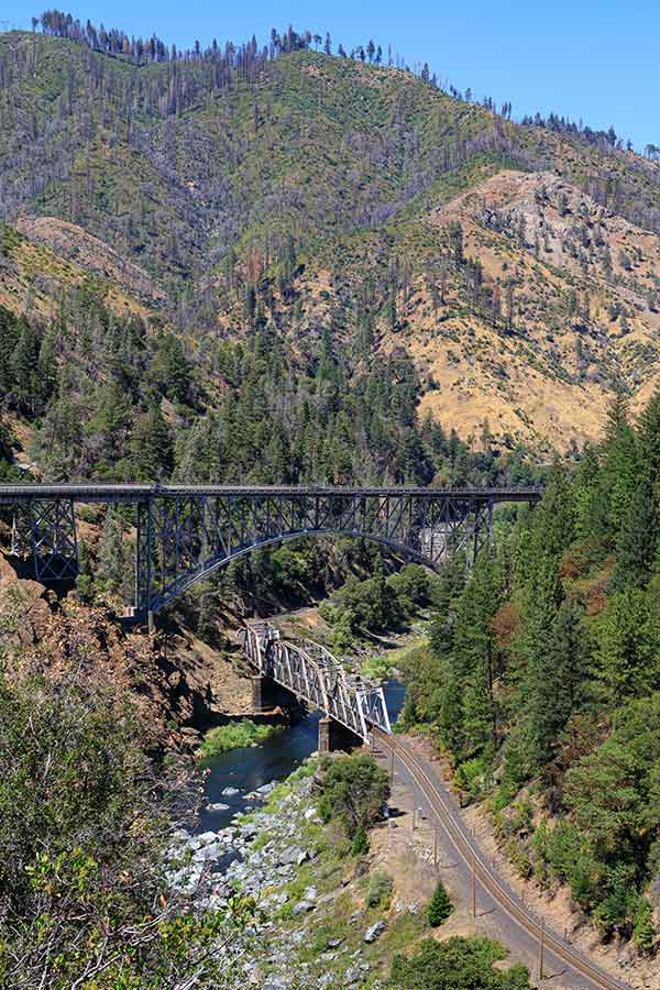 Two bridges span a river, surrounded by trees and mountains