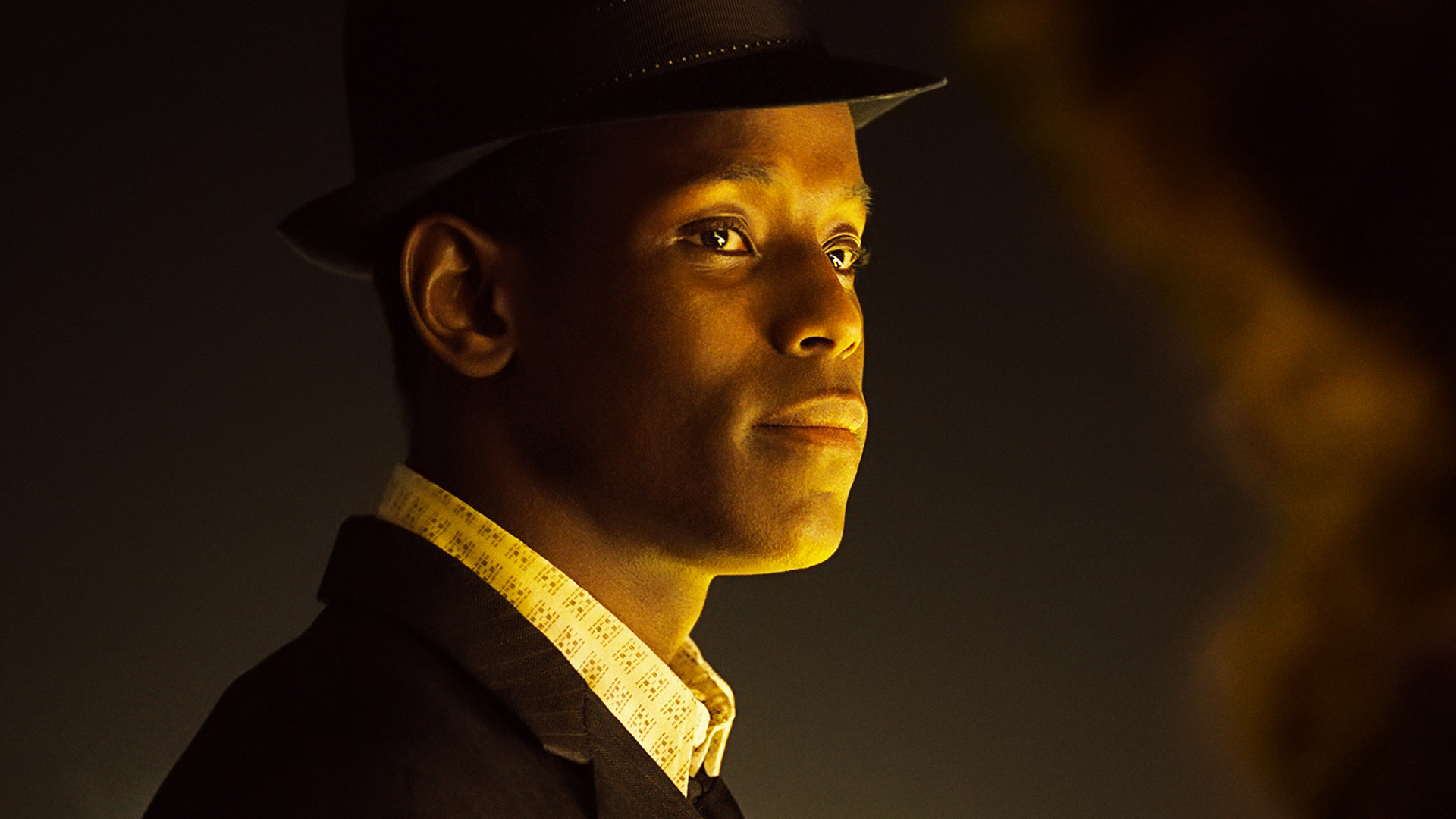Young Black man in suit and hat lit by golden light