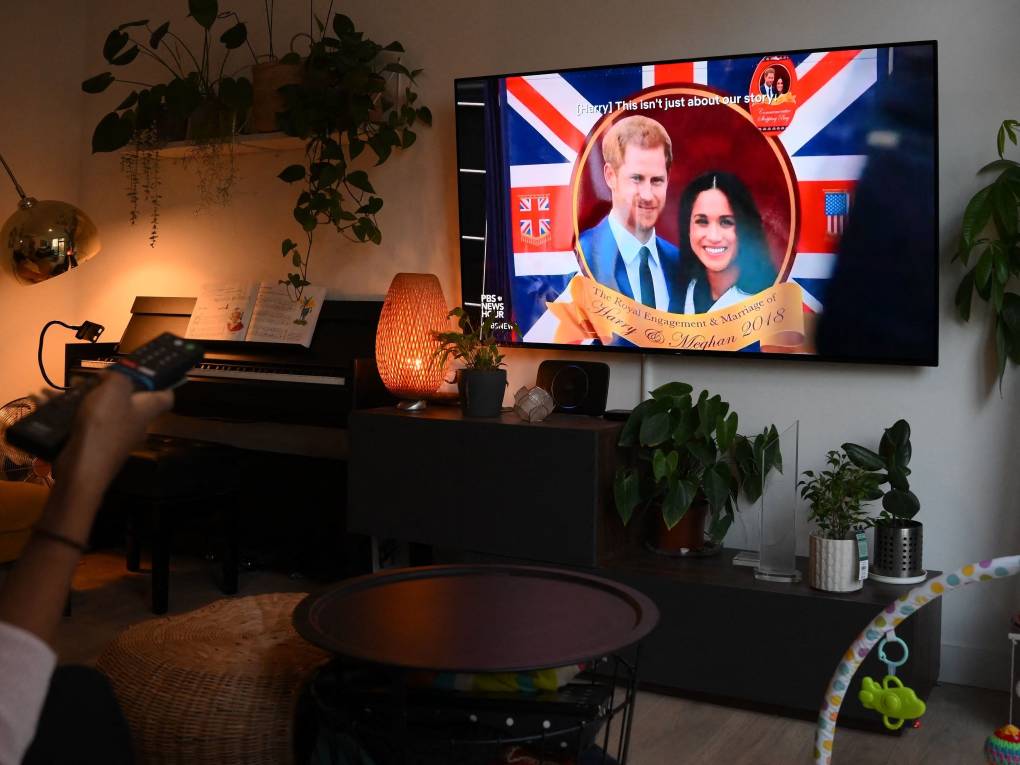 A wall-mounted television with an image of Prince Harry and Meghan Markle on it, in an average living room.
