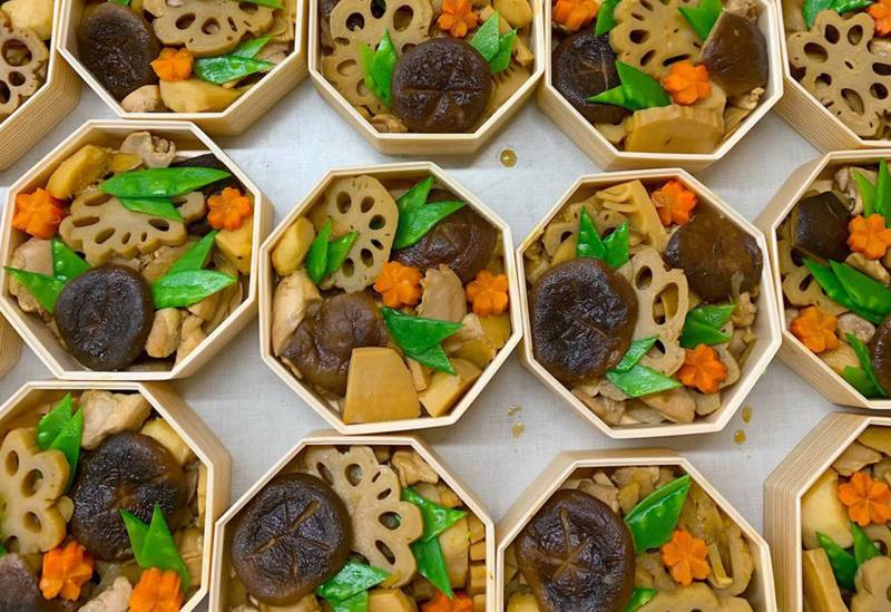 Overhead view of wooden Japanese New Year's boxes filled with simmered chicken and root vegetables.