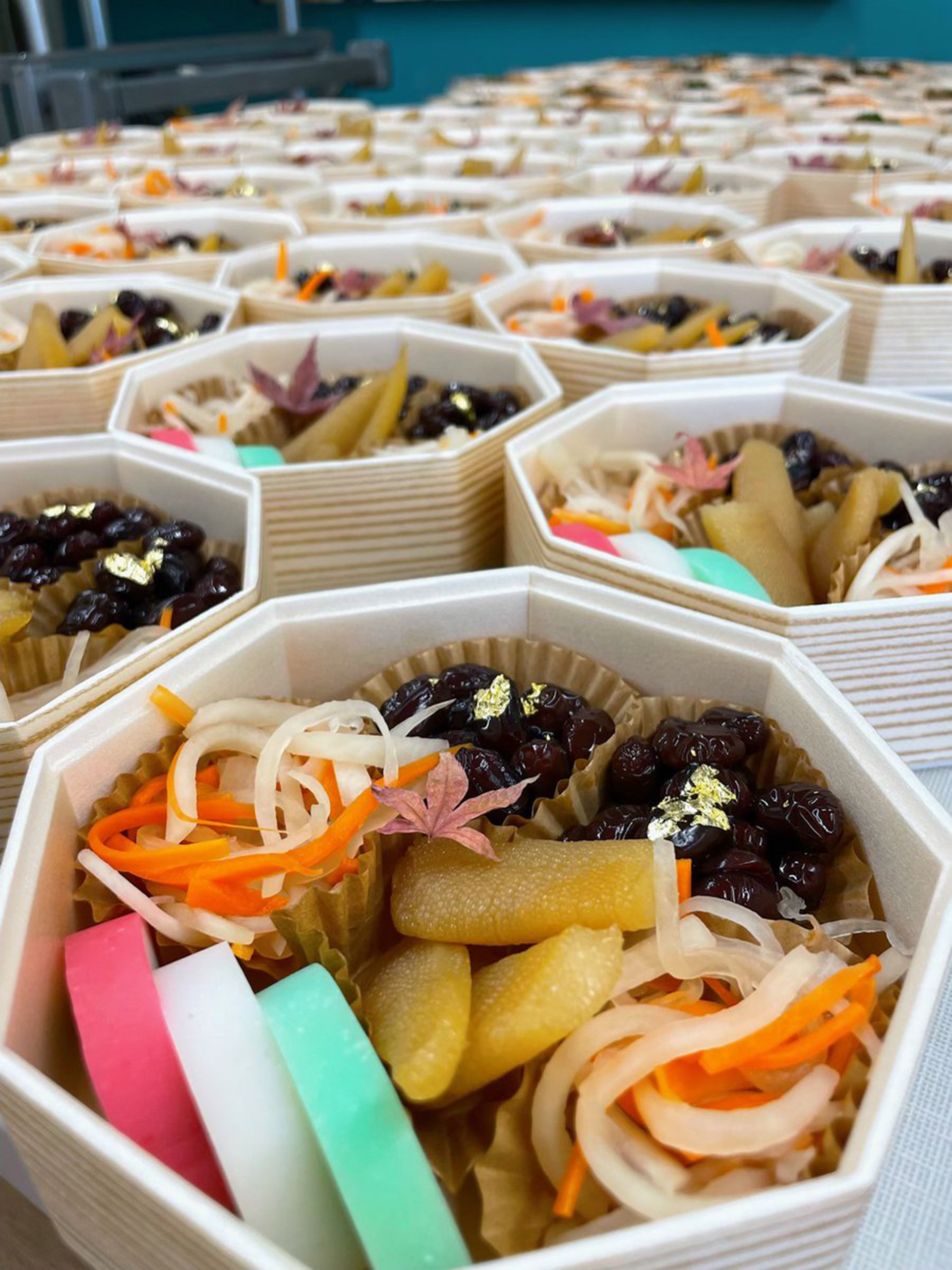 Many wooden boxes filled with traditional Japanese New Year's dishes, including colorful fish cakes, daikon and carrot salad, and sweet black soybeans.