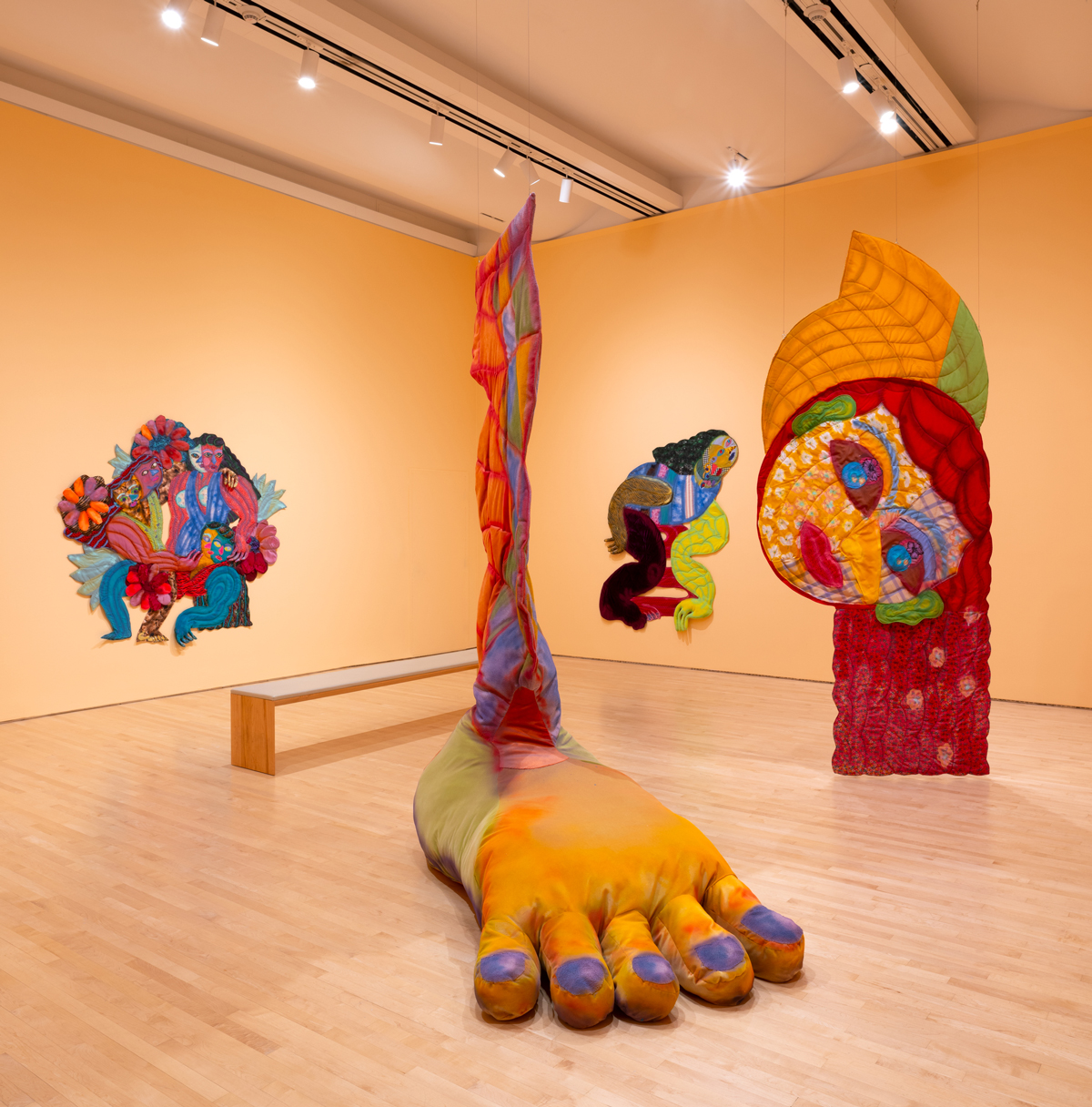 Light peach walls and arrangement of large multicolored textile works with giant foot and smiling head