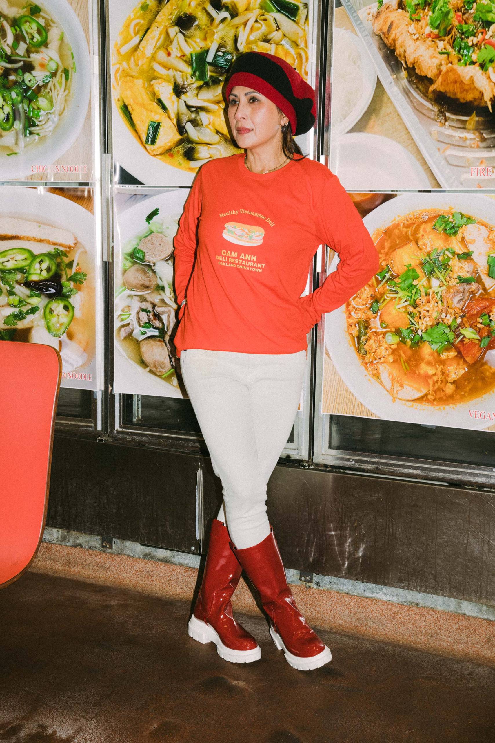 Anh Nguyen poses in a poppy orange long-sleeved tee and a stylish hat and boots, inside her restaurant Cam Anh.