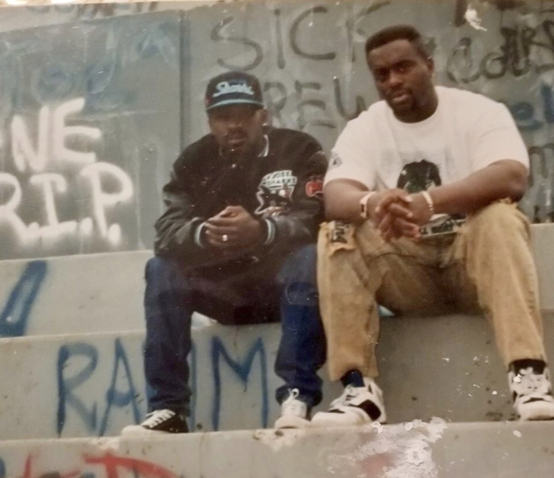 Two young men sit on graffiti-covered steps, looking into the camera