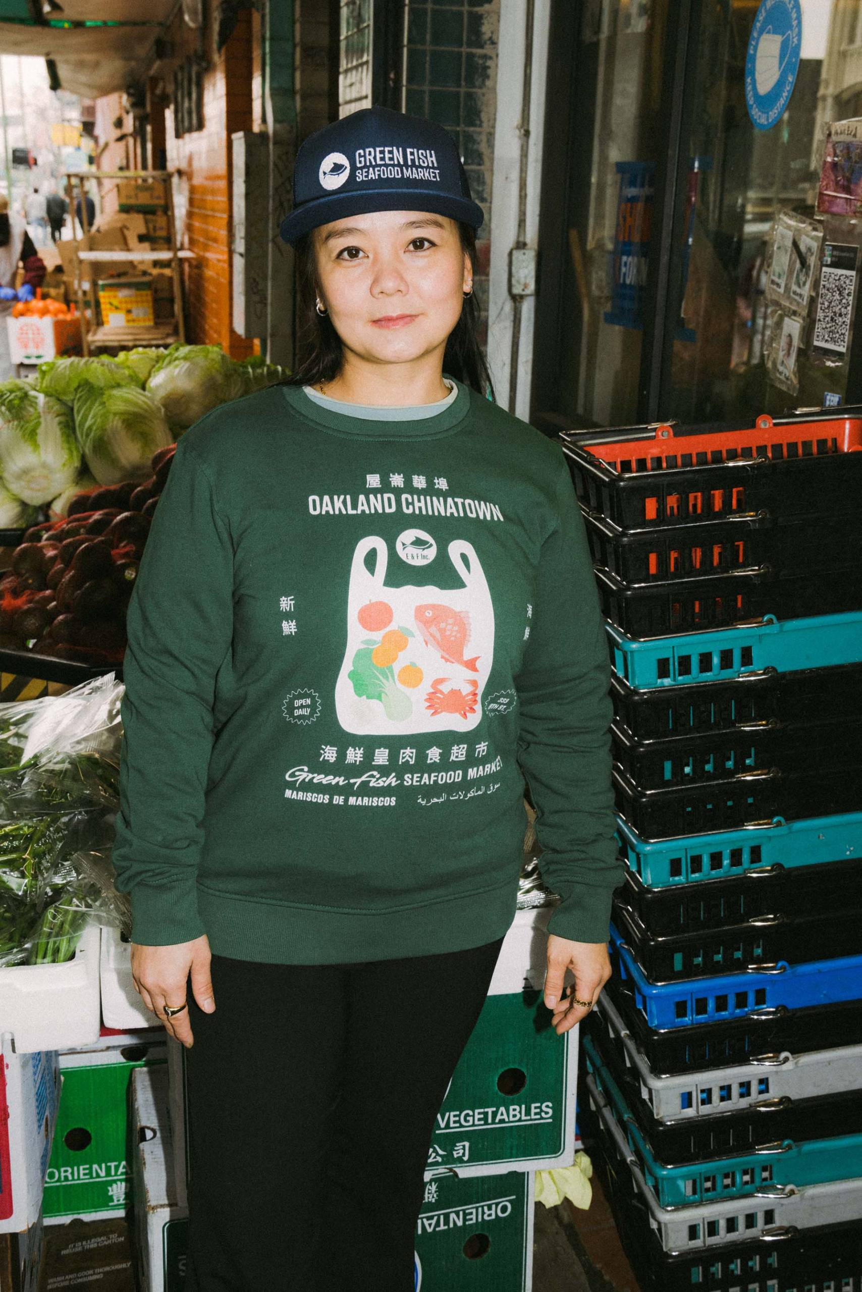Woman poses in a trucker hat and a green sweatshirt, both promoting her business, Green Fish Seafood Market.