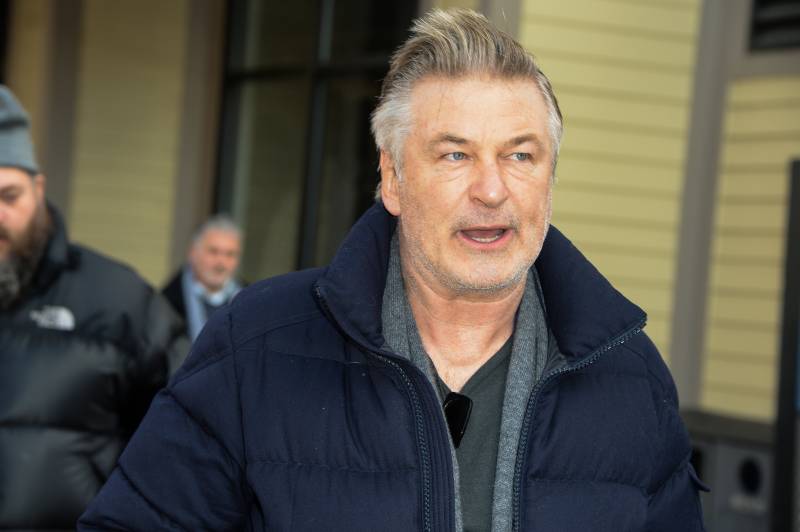 A middle-aged white man with striking grey hair talks while walking, wearing a winter coat.