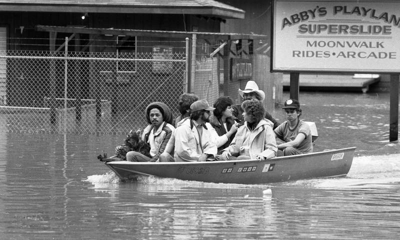 Eight people and a dog travel in a small motorboat in front of a sign that reads "Abby's Playland."