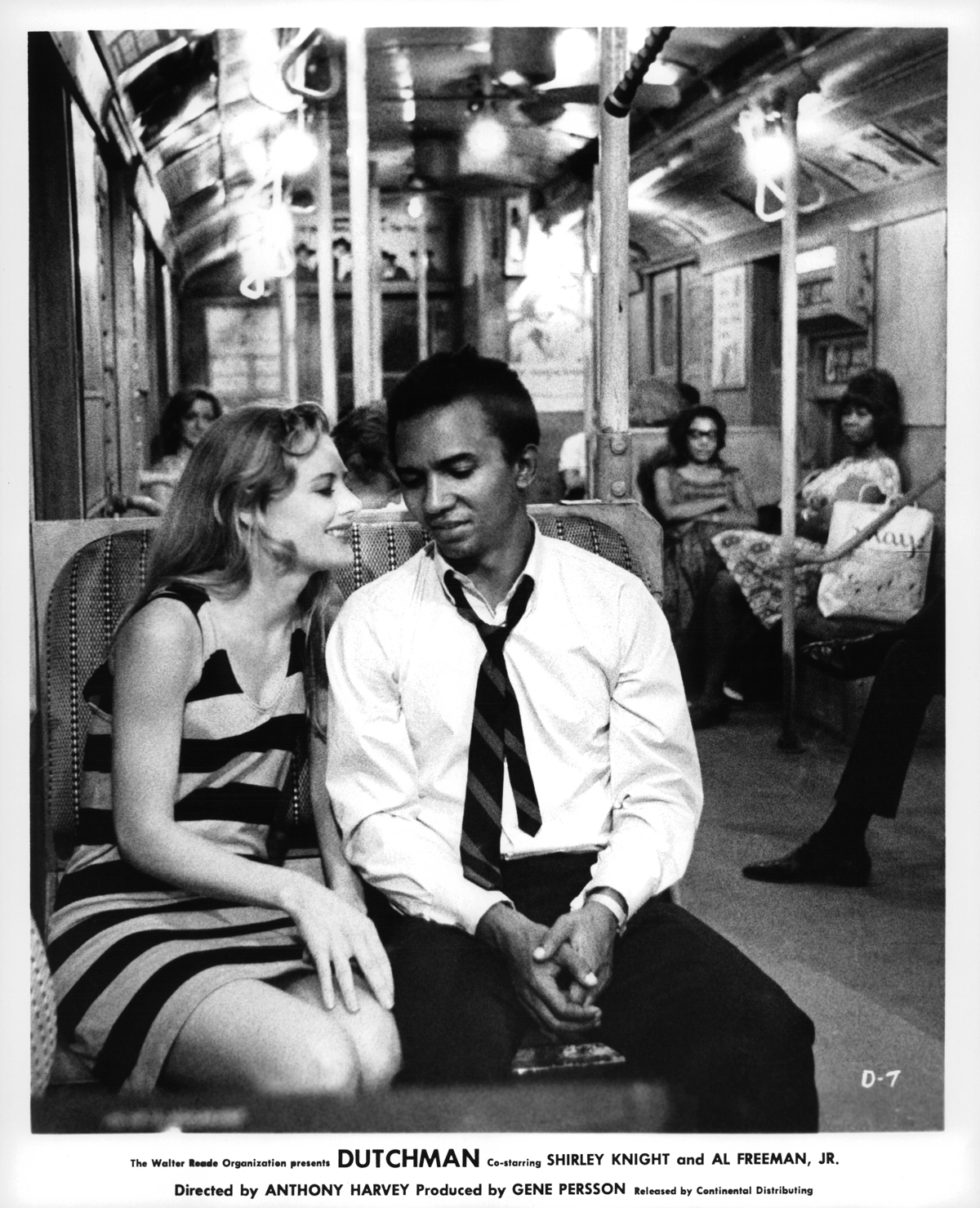 Black-and-white image of a white woman talking to a Black man in a subway car, people in background