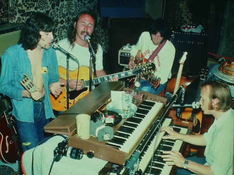 a four-piece band of white men with long hair record music in a studio in the 1970s
