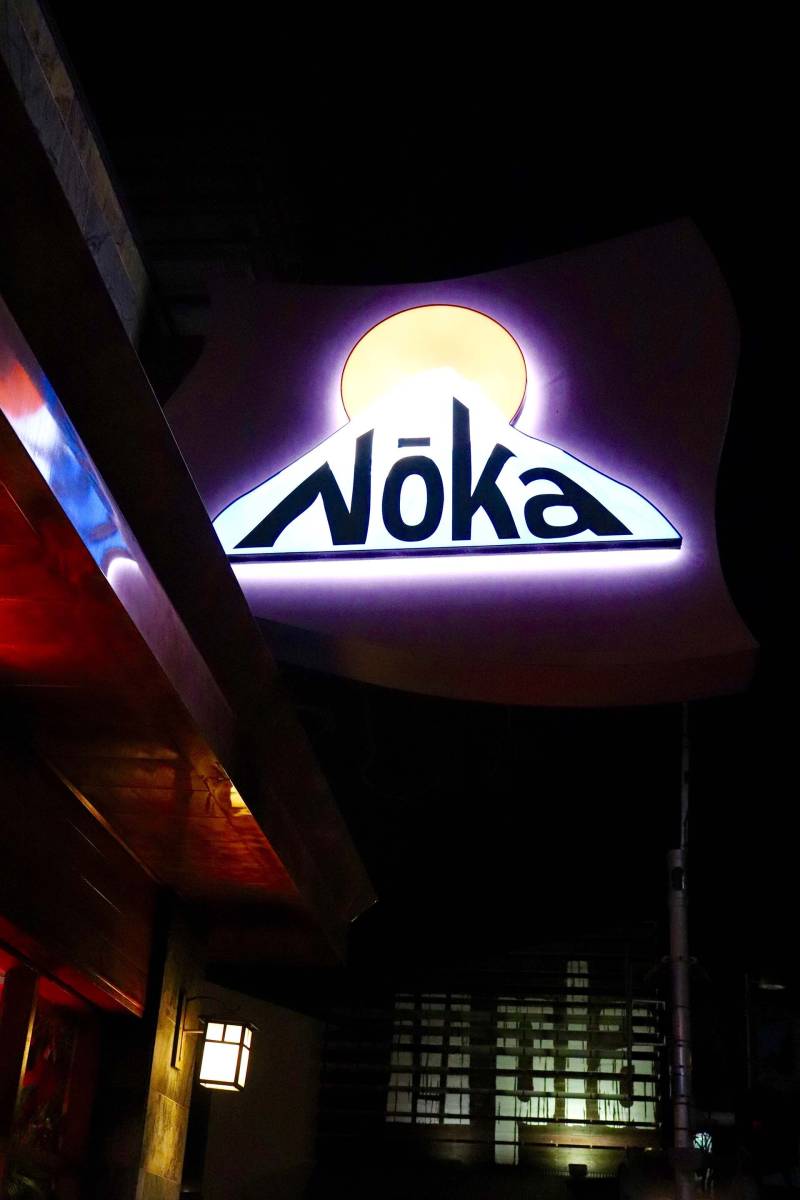 a neon "Noka" sign hangs in front of the restaurant at night