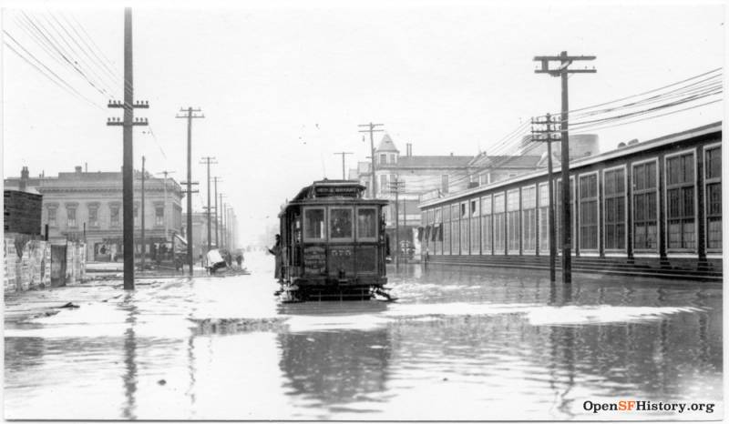 Black and white image of classic San Francisco trolley running through an empty flooded street.