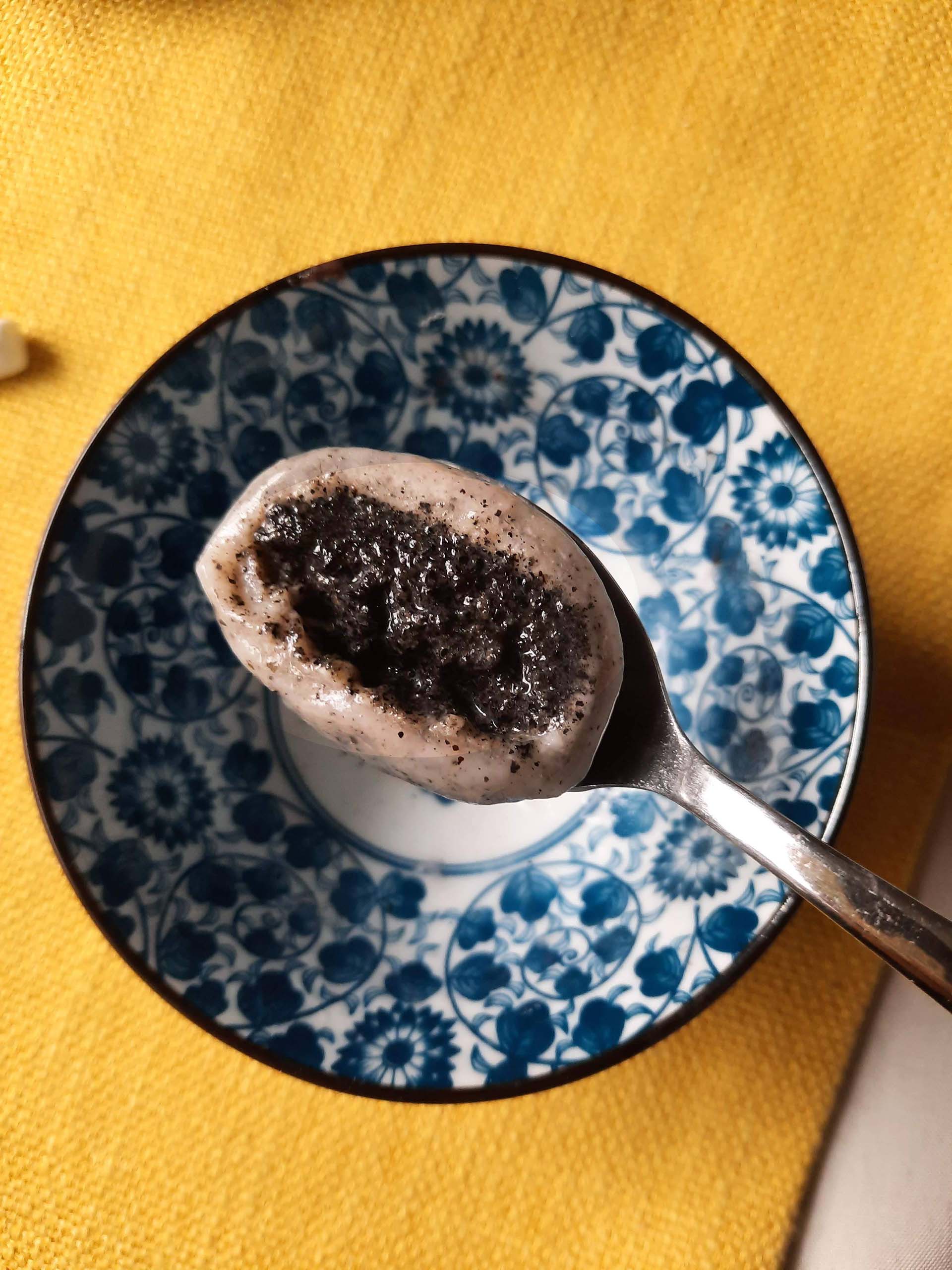 Cross section of a tangyuan (glutinous rice ball) on a spoon, with the black sesame filling visible.