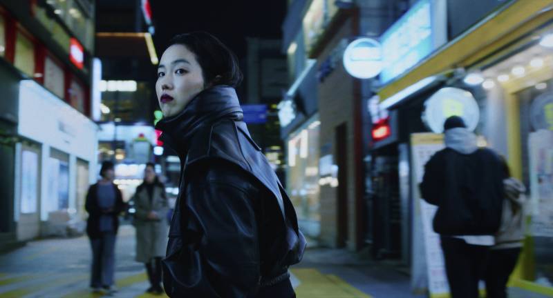 Young Asian woman in dark lipstick stands on busy brightly lit street