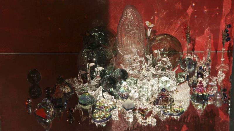 Collection of sparkling glass objects, including a Virgin Mary statue in a red cabinet space.