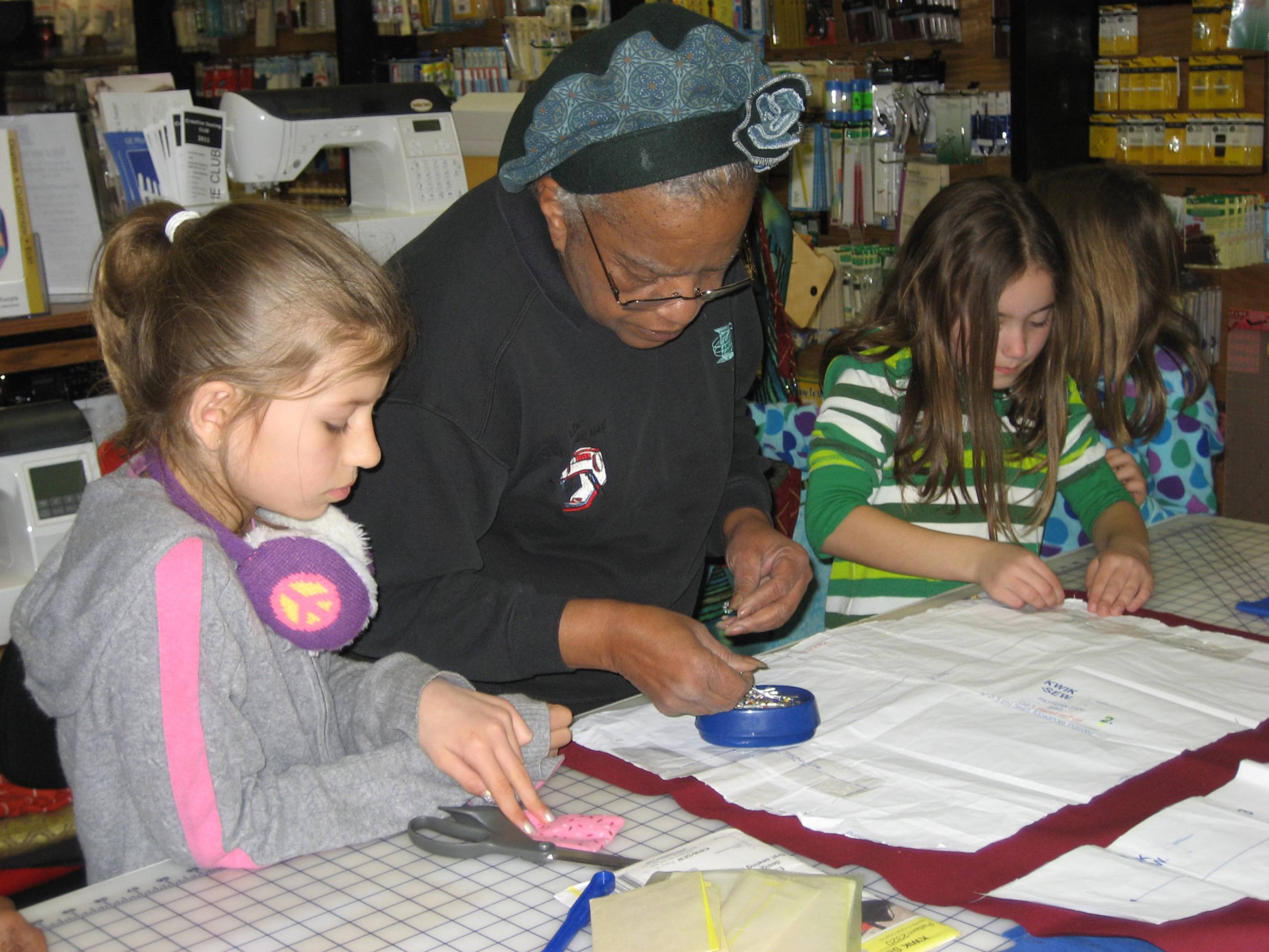 Older Black woman works with two kids to pin pattern to red fabric
