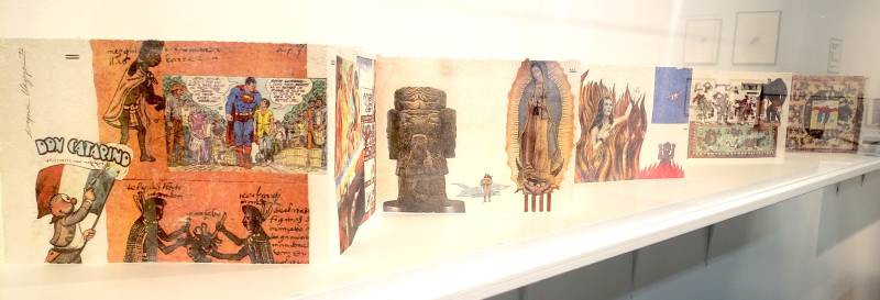 A folded out booklet inside a display case shows traditional Mexican artwork and American cartoons.