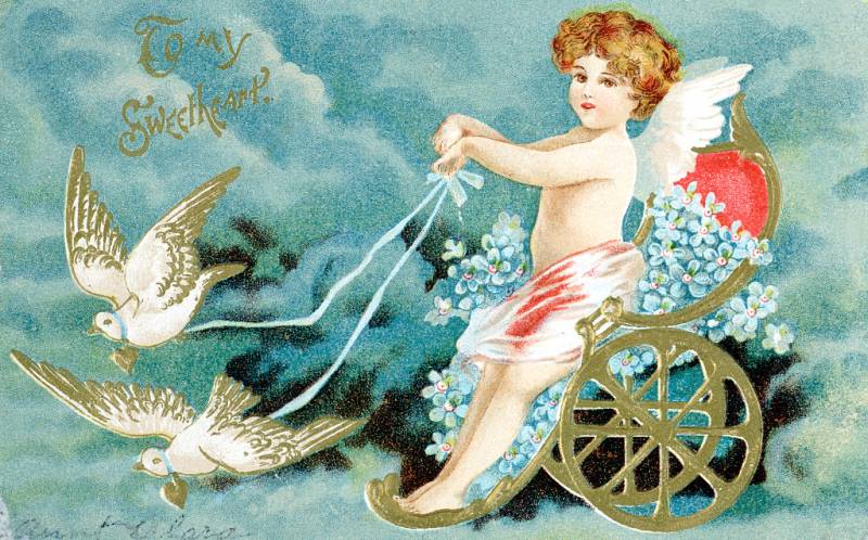 A greeting card featuring an illustrated cherub sitting in a golden carriage being pulled by white birds across a blue sky.