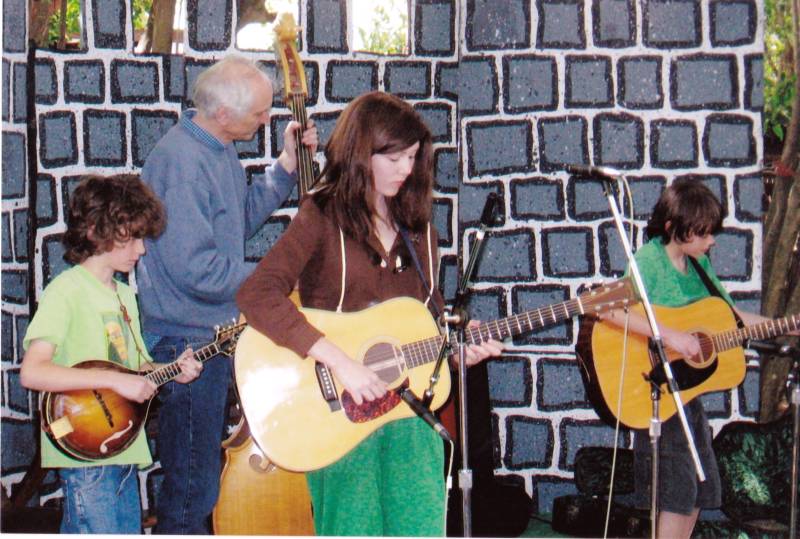a four piece band, an older man with white hair and three kids, one girl and two young boys, all playing guitar