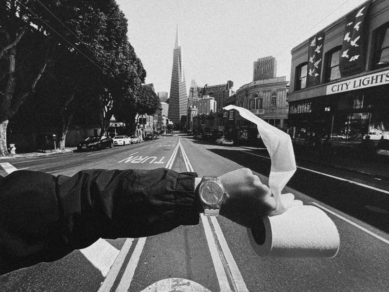 Black-and-white image of hand holding roll of toilet paper on empty street leading to Transamerica Pyramid