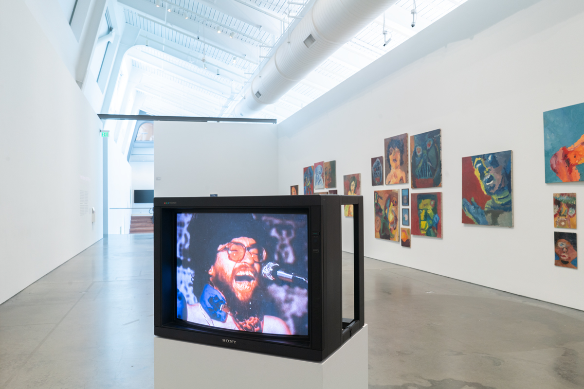 Gallery view with TV in front center, white man with beard and glasses open-mouth on screen