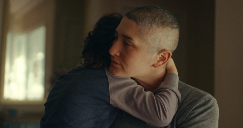 A white woman with buzzed hair hugs a child