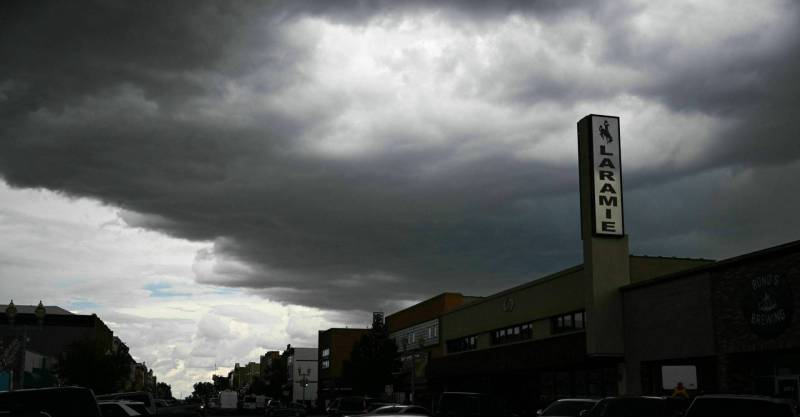 Dark gray clouds spread out on a long row of store fronts. One displays a vertical sign that says LARAMIE.