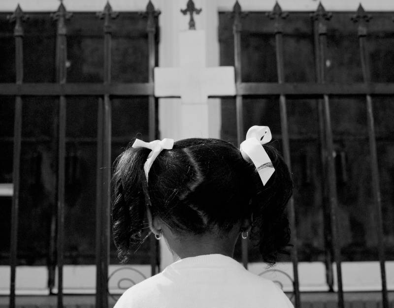 Black-and-white image of back of Black girl's head with white cross above.