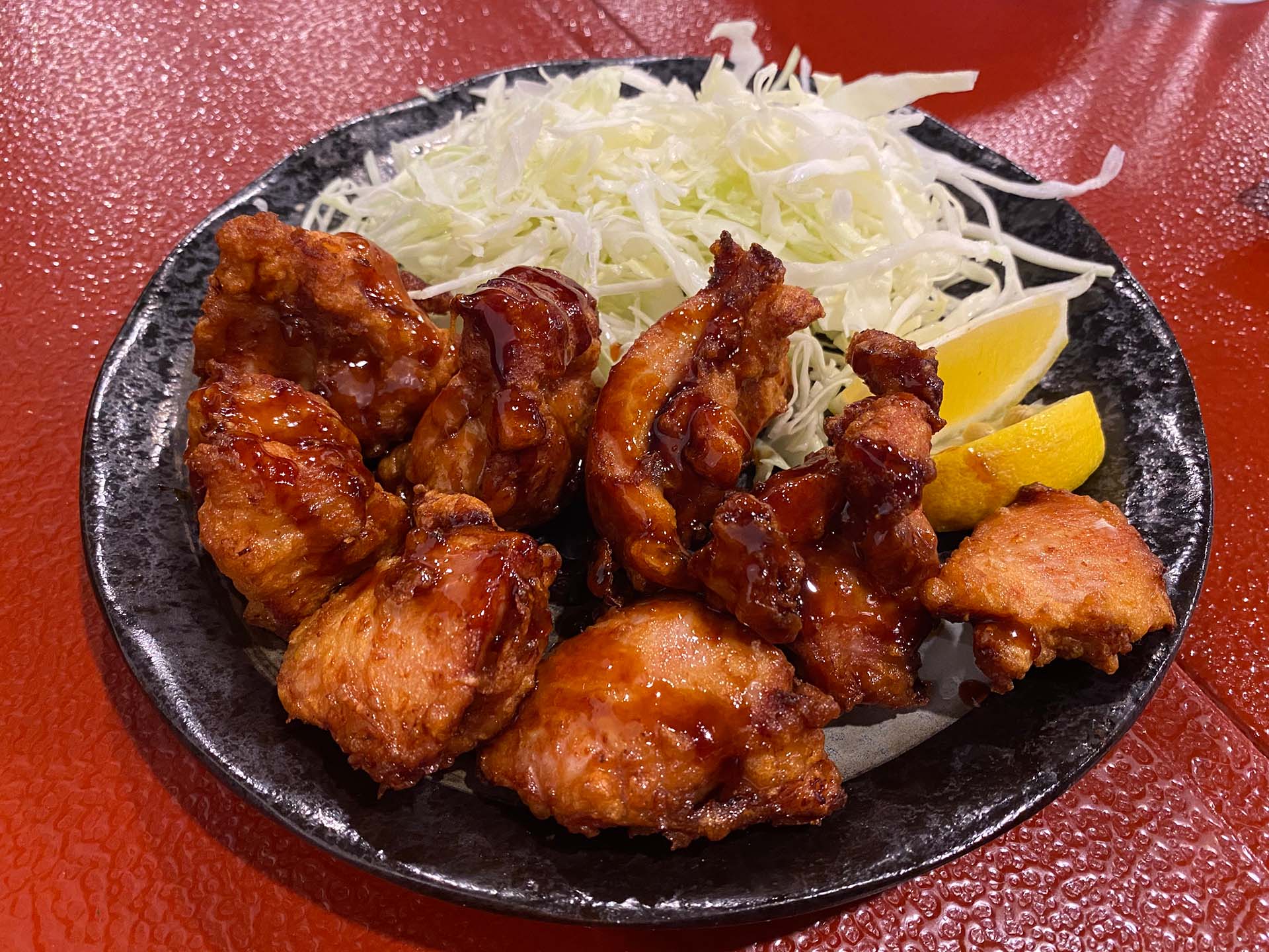A plate of Hawaiian-style mochiko fried chicken with shredded cabbage and lemon wedges on the side.