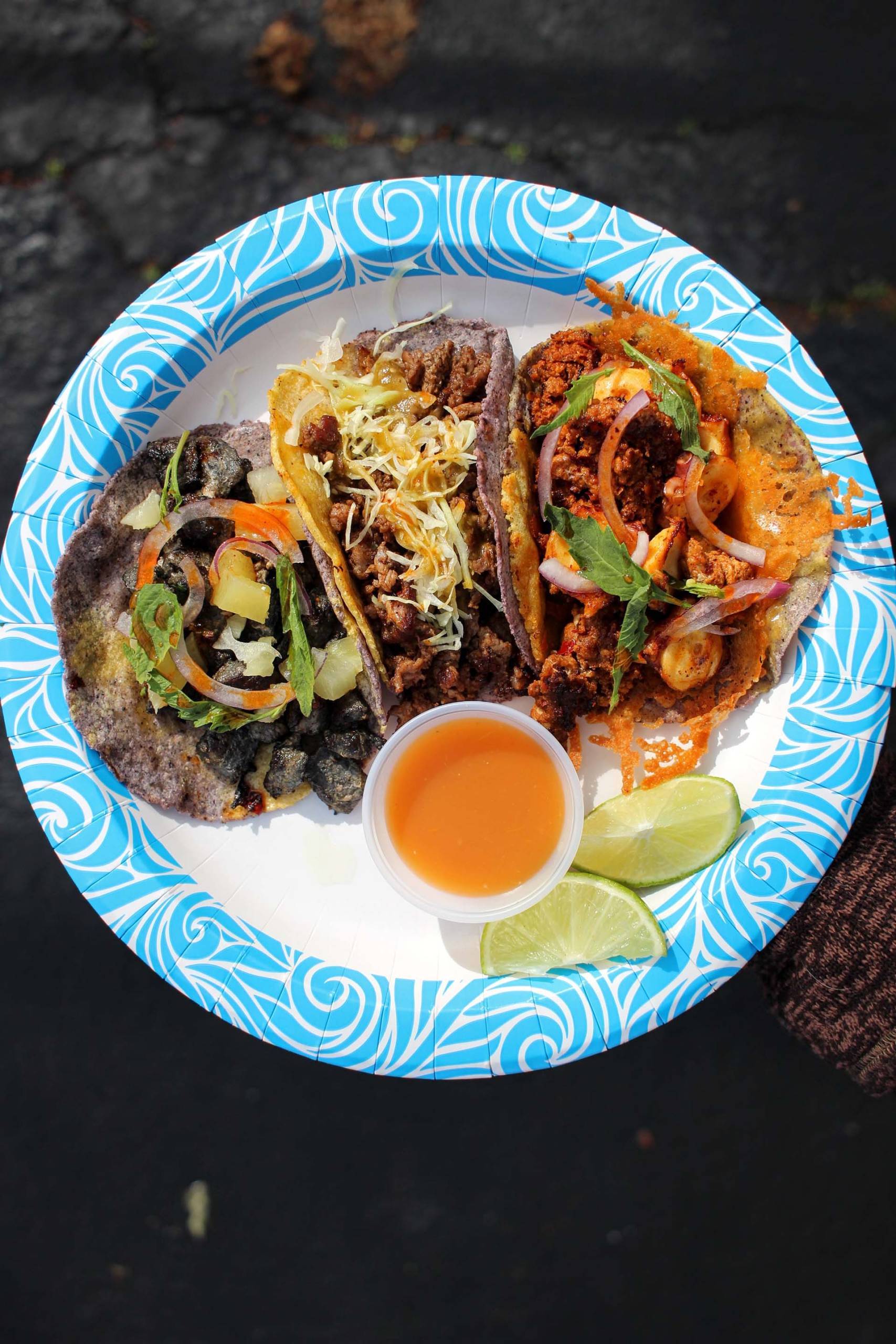 Overhead view of a plate of four tacos, with a side of bright orange salsa.
