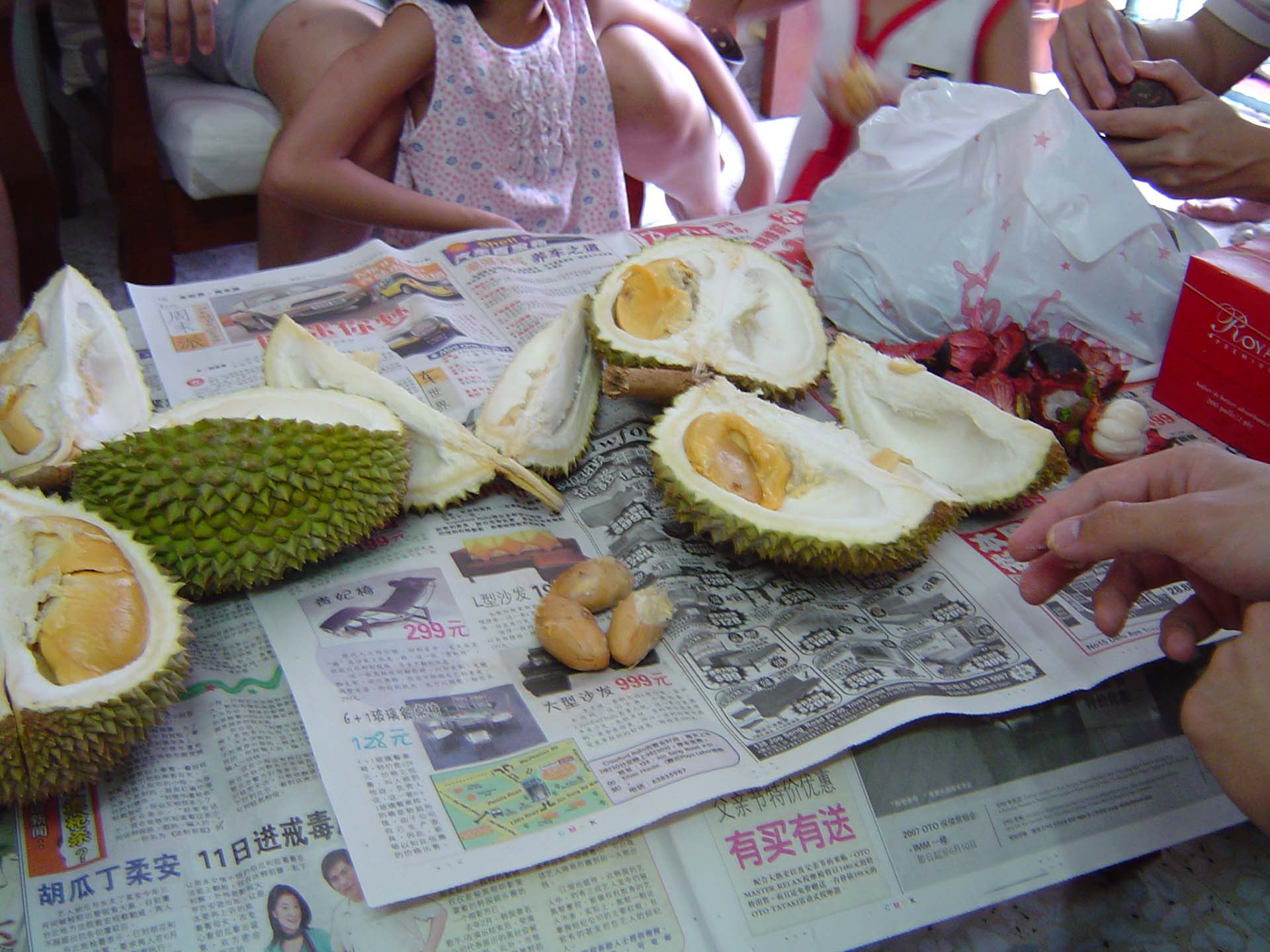 A spread of split durian, still in its spiky green rind, spread on top of sheets of newspaper.