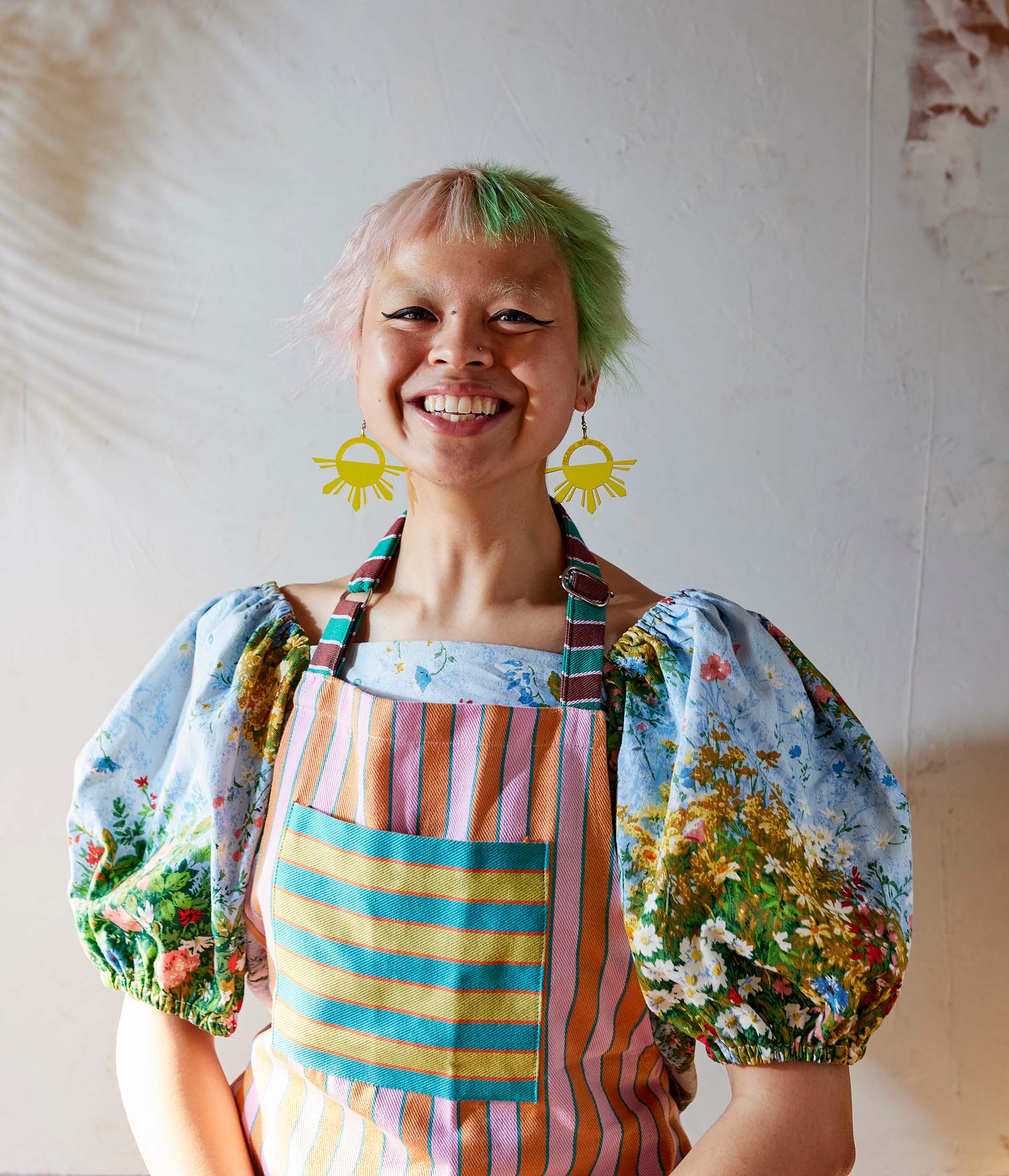Portrait of cookbook author Abi Balingit, who wears a colorful apron that matches her pink and green hair.