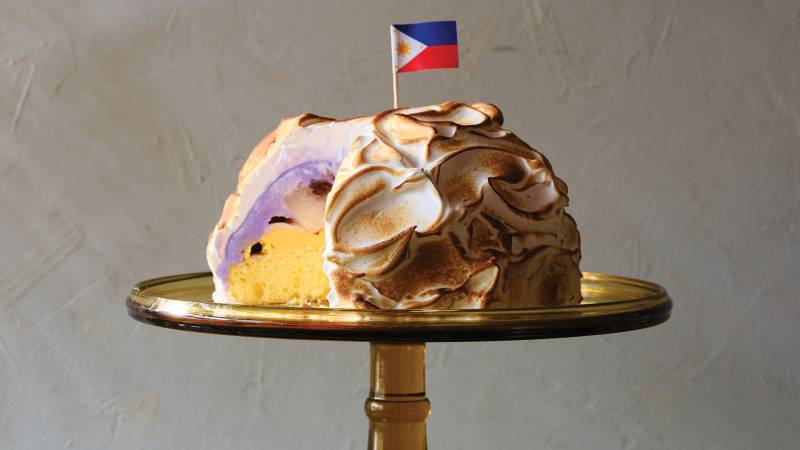 A baked Alaska dessert with a small Filipino flag inserted on top, displayed on a cake stand.