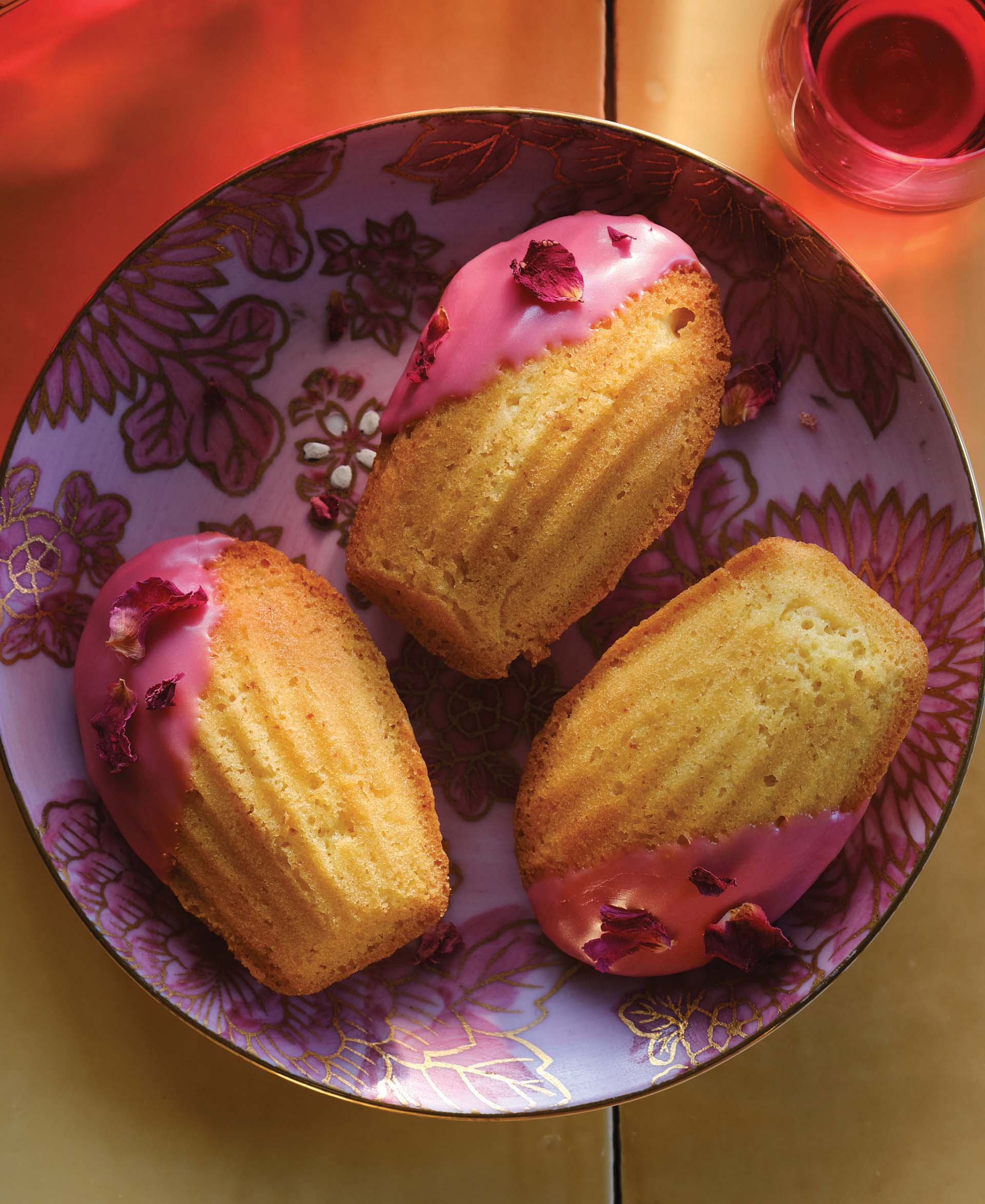A bowl of madeleines topped with dried rose petals and a purple-pink hibiscus glaze.