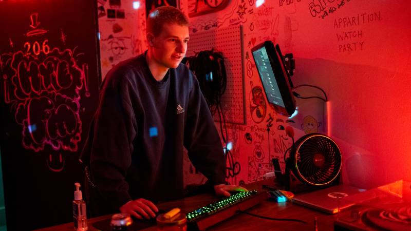 White man in red-lit room uses mouse and keyboard with graffiti on walls