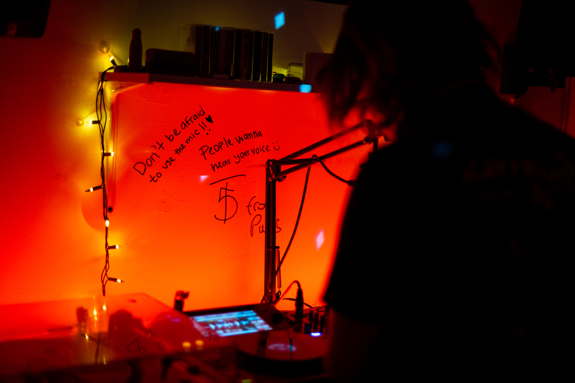 Writing on red-lit wall reads "Don't be afraid to use the mic!! People wanna hear your voice"
