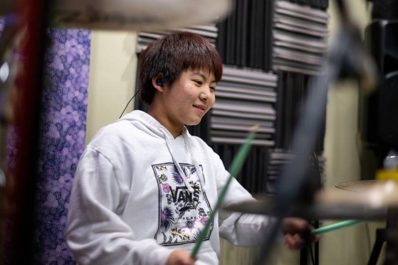 a young Japanese girl plays the drums while smiling