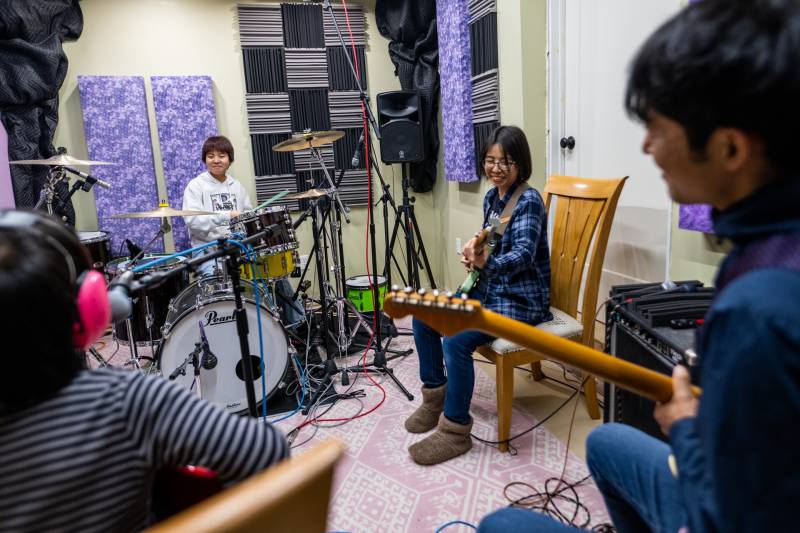 a four-person Japanese family sit in a home music studio practicing instruments and smiling
