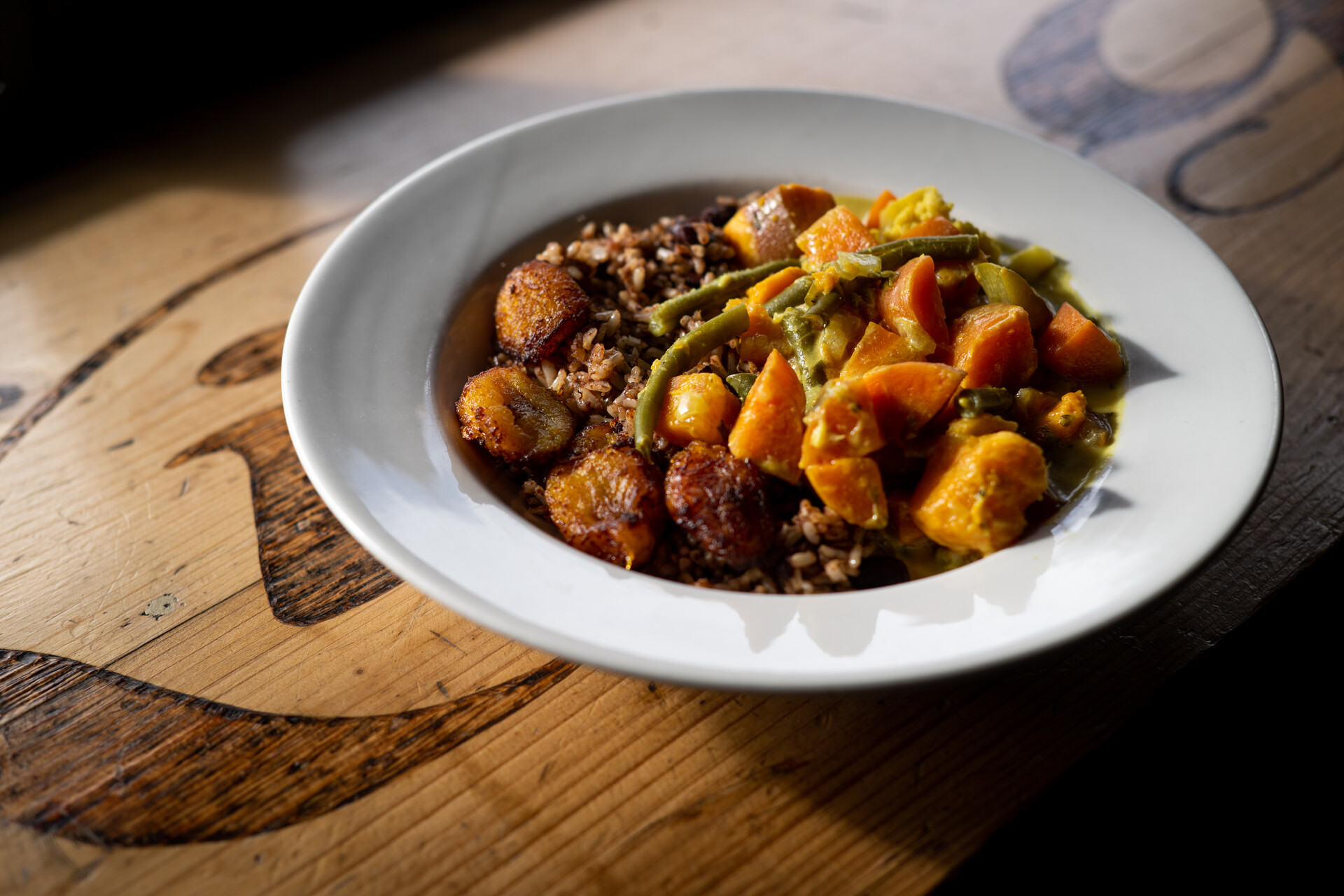 A plate of Jamaican-style vegetable curry, served over rice and peas, on a wooden tabletop. 