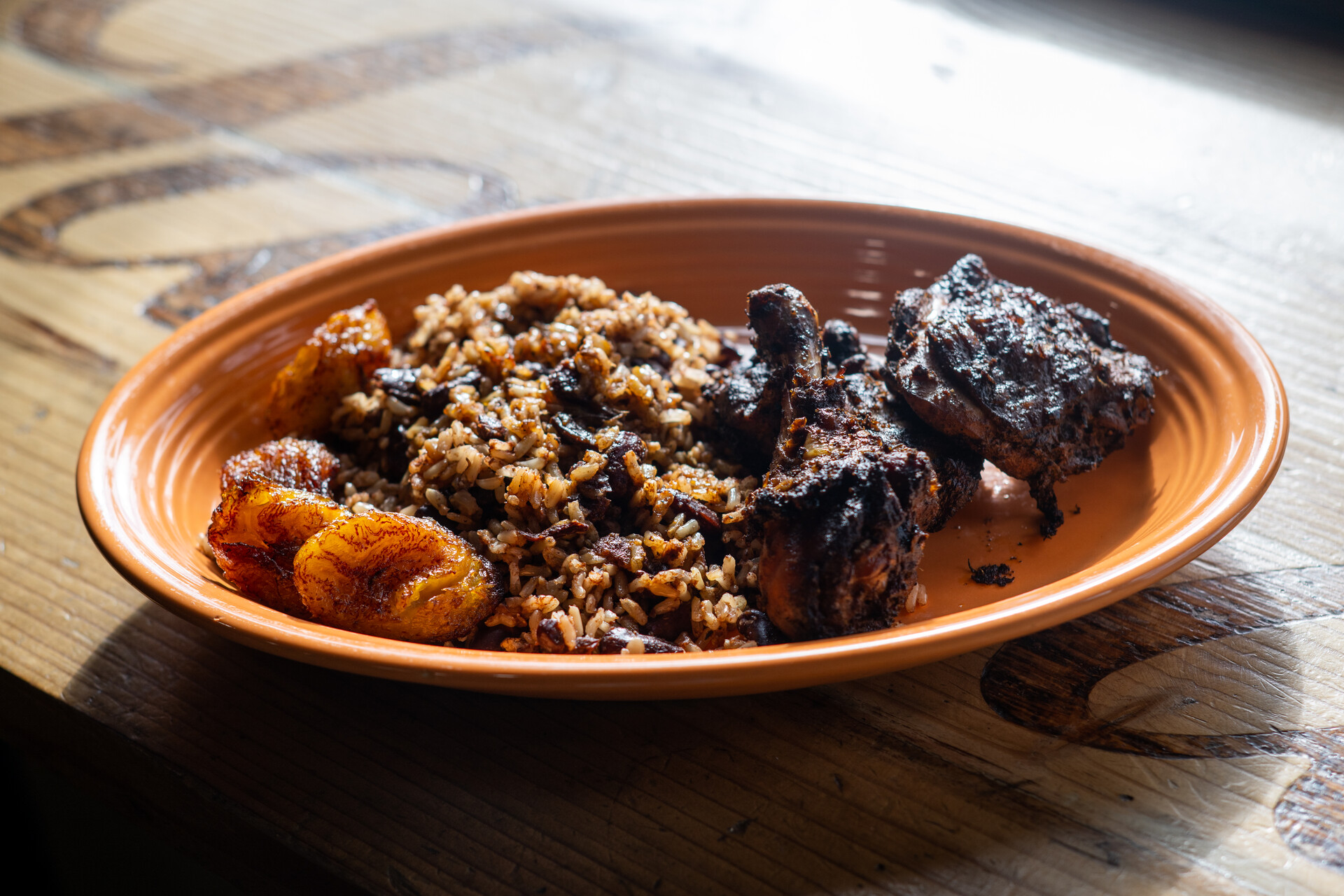 A plate of jerk chicken, served with plantains and rice and peas. 
